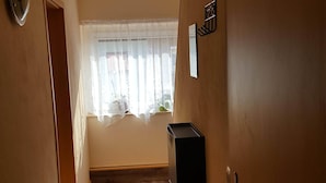 A narrow hallway with a wooden floor, a door on the right, and a window with sheer curtains.