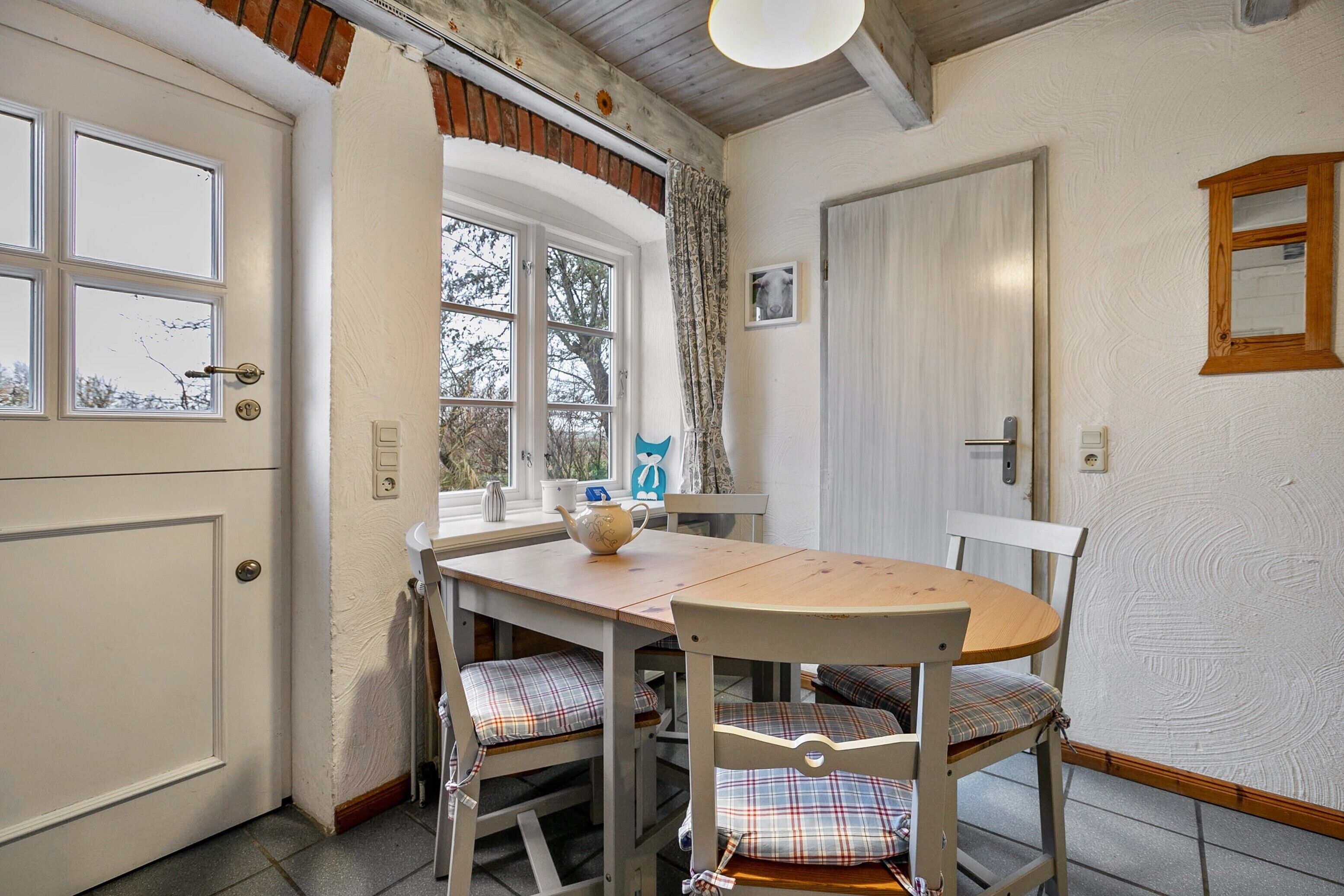 Un coin repas avec une table et des chaises en bois, une fenêtre avec des rideaux et une porte.