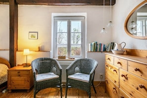 A room with wicker chairs, a wooden dresser, a window with a view, and a lamp on a nightstand. - Apartment 'Ferienwohnung 3' with Shared Garden, Balcony and Wi-Fi (Rodenäs)