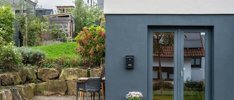 A modern building with a grey facade, a door with glass panels, and a small outdoor seating area with a table and chairs.
