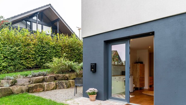 Una casa moderna con fachada gris, un muro de contención de piedra, un camino de grava y una planta en maceta.