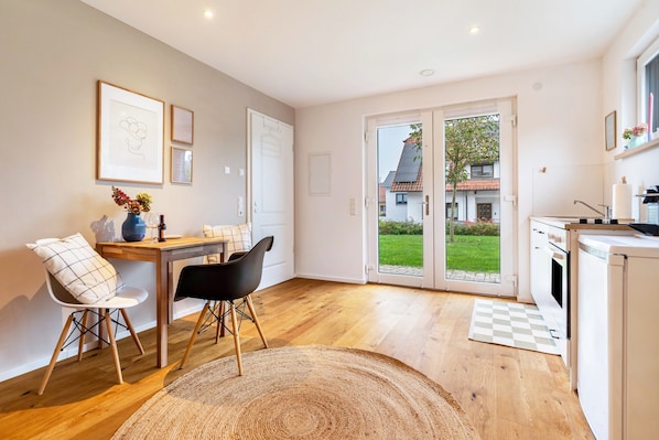 A modern kitchen with a dining area, wooden flooring, and a view through the glass door.