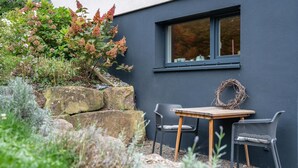Un área de estar moderna al aire libre con una mesa y sillas, un adorno festivo y una ventana con vista a un jardín lleno de plantas.