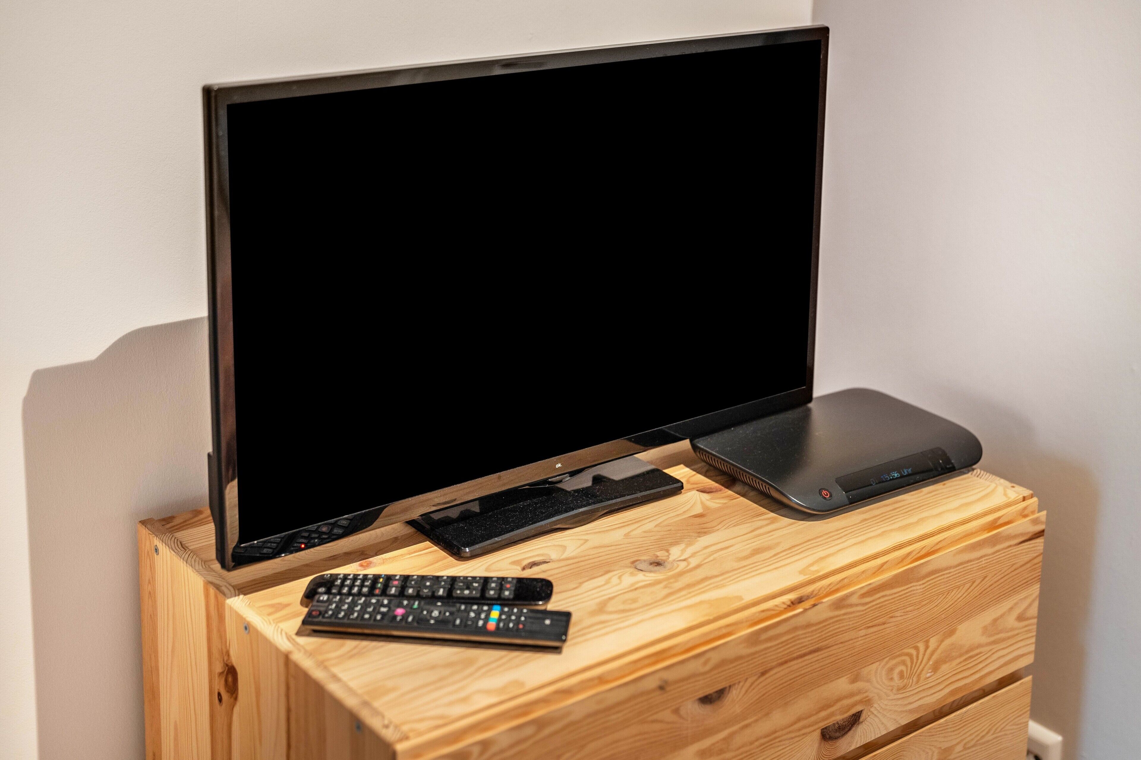 A wooden TV stand with a flat-screen TV, a keyboard, and a remote control.