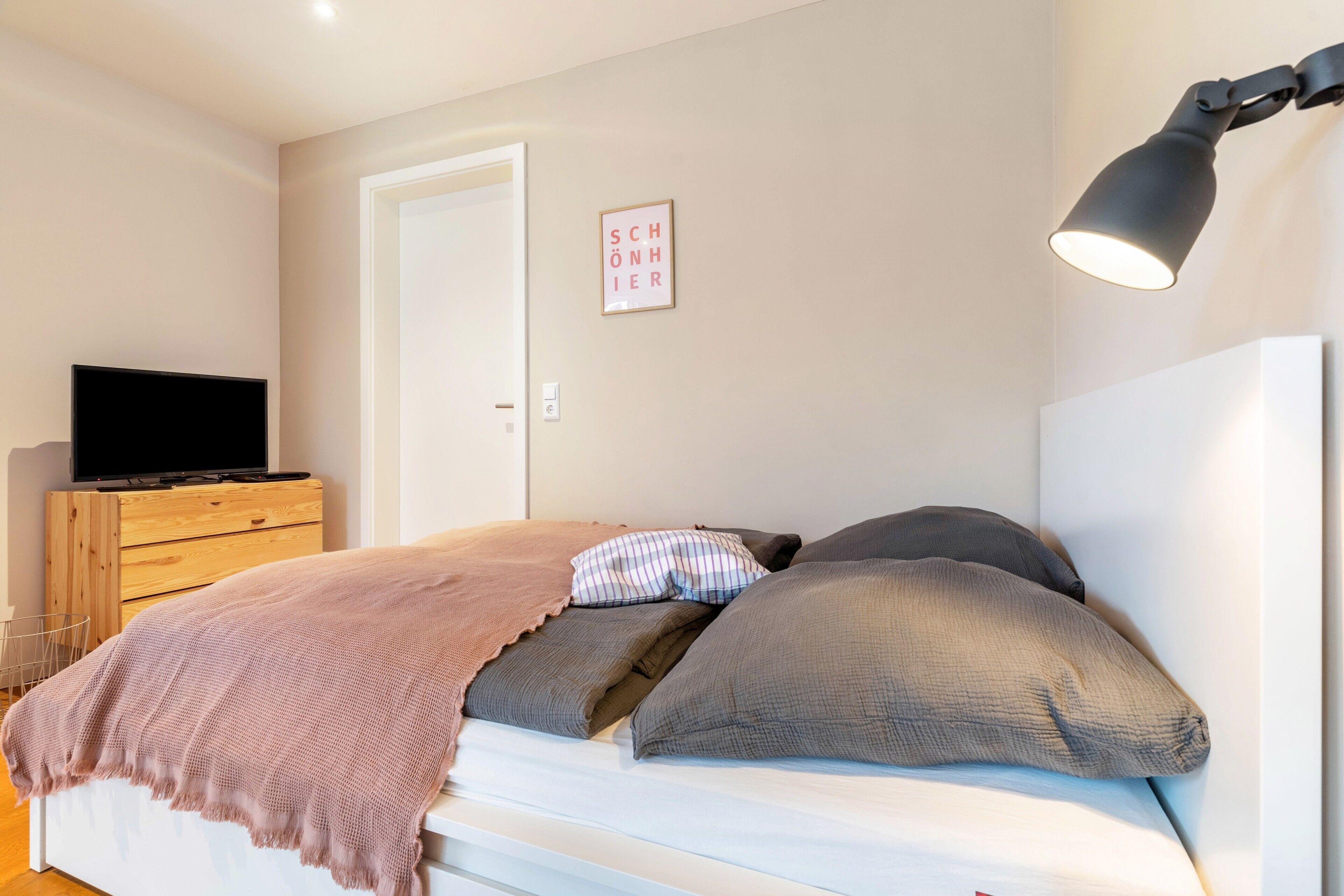 Een slaapkamer met een bed, een televisie op een dressoir, een wandlamp en een lijst met een bord.