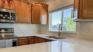 A kitchen with wooden cabinets, a stainless steel range, a double sink, and a window with blinds.