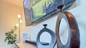 A modern interior with a flat-screen TV mounted on a wall, a wooden console table with decorative metal rings, and a potted plant.