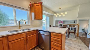 A modern kitchen with wooden cabinets, a built-in dishwasher, a large island, and a dining area with a chandelier.