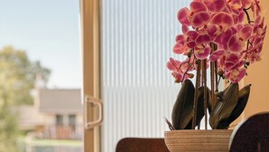 A dining table with a potted orchid, two chairs, and a view through a window.