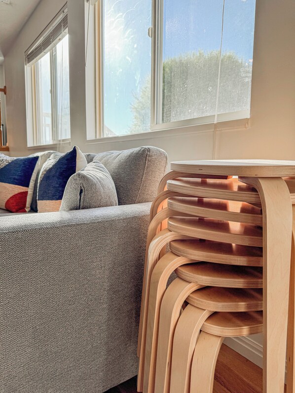 A modern living room with a grey sofa, a wooden side table, and large windows with blinds.