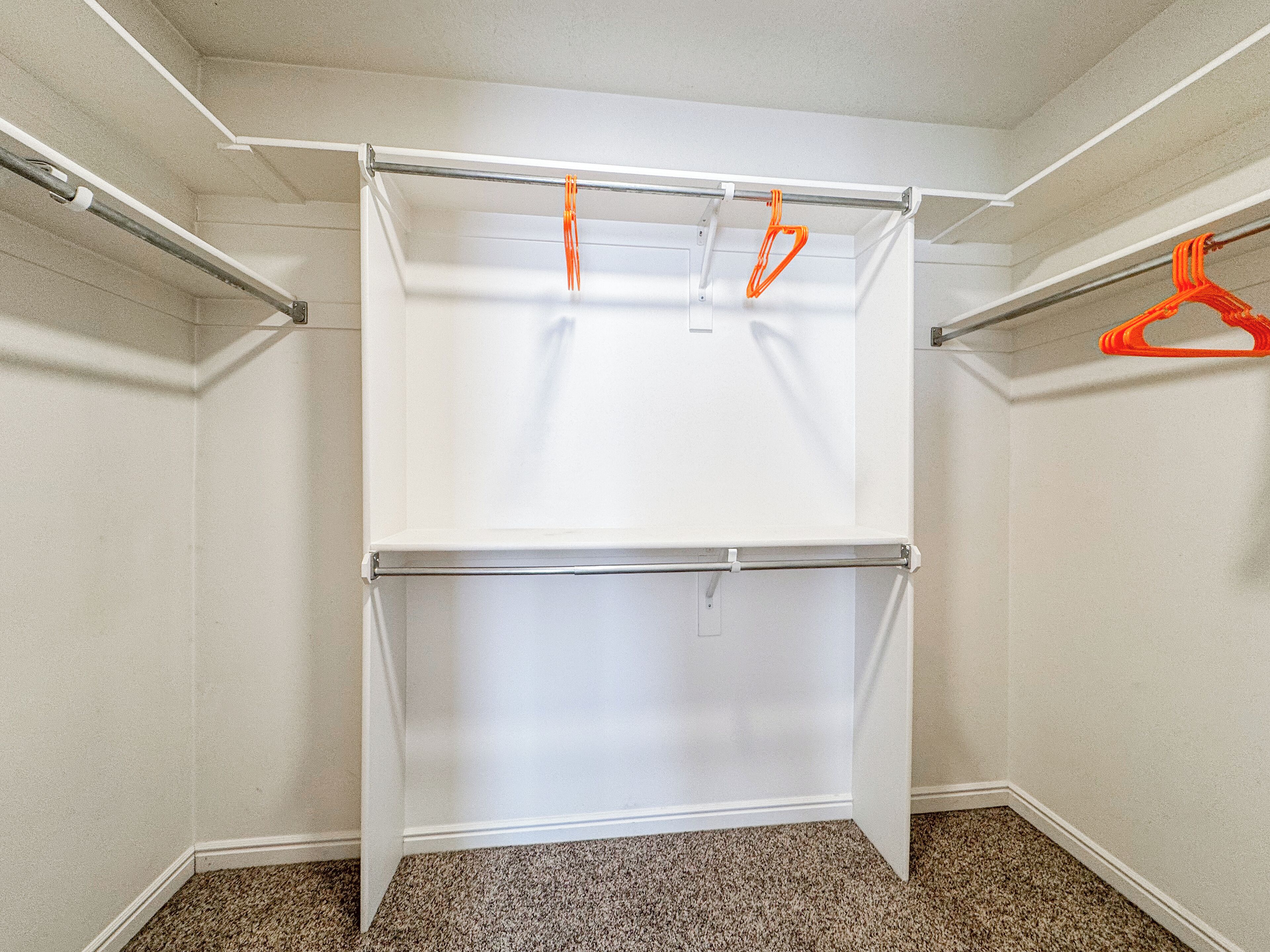 A walk-in closet with a white hanging rod and a white shelf unit.
