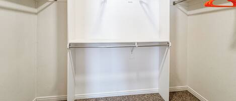 A walk-in closet with a white hanging rod and a white shelf unit.