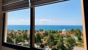A window with a view of a coastal town, a clear sky, and the ocean. - Mersin Panorama Otel (Erdemli)