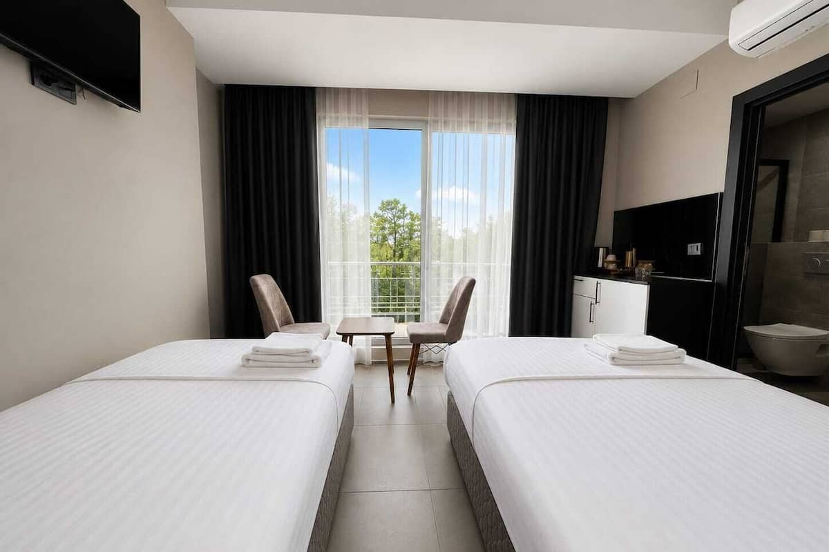 A hotel room with two beds, a small table, chairs, a TV, and a balcony with curtains.
