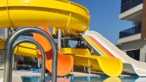 A swimming pool with multiple slides, including a rainbow-colored one, and a modern building in the background. - Mersin Panorama Otel (Erdemli)