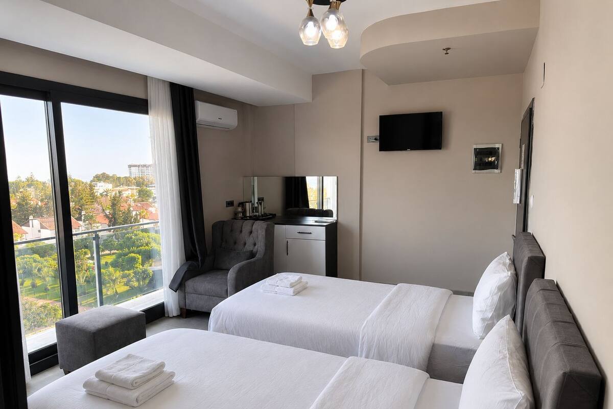 A hotel room with two beds, a desk, a chair, a TV, and a balcony with a view.