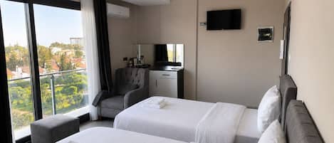 Quarto de hotel com duas camas, uma escrivaninha, uma cadeira, televisão e varanda com vista.