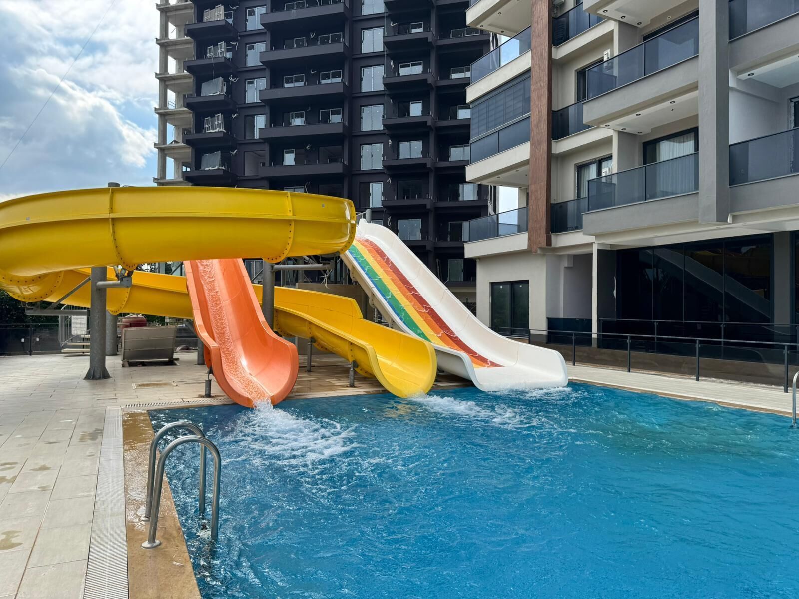 A swimming pool with multiple slides and a modern apartment building in the background.