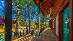 A wooden porch with a green railing, a green door, and a welcome sign. - Sunset Summits Cabin | Hot Tub | Game Room | (Oakhurst)