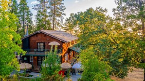 A rustic cabin with a wooden exterior, a balcony, and a thatched roof structure. - Sunset Summits Cabin | Hot Tub | Game Room | (Oakhurst)