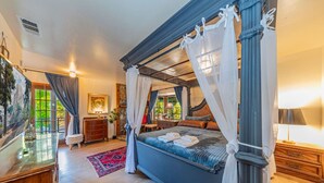 A spacious bedroom with a four-poster bed, a large window with curtains, a nightstand, and a dresser. - Sunset Summits Cabin | Hot Tub | Game Room | (Oakhurst)
