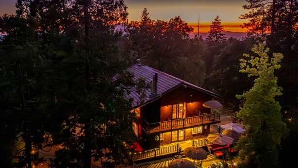 A cabin with a balcony, surrounded by trees, during sunset. - Sunset Summits Cabin | Hot Tub | Game Room | (Oakhurst)
