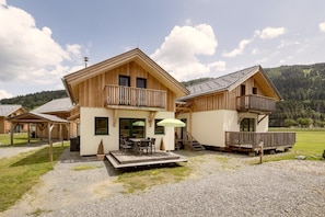 A wooden chalet with a balcony, a covered patio, and a view of the surrounding forest. - Classic chalet with infrared sauna (Murau)