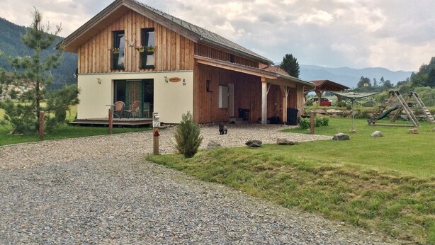Eine Holzhütte mit Kiesauffahrt, einer Veranda und einem Berg im Hintergrund.