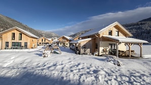 Eine Reihe von Holzhütten mit schneebedeckten Dächern, vor einer Berglandschaft gelegen.