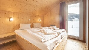 Ein Zimmer einer Holzhütte mit einem Bett, zwei Nachttischen und einem Fenster mit Blick auf eine verschneite Landschaft.