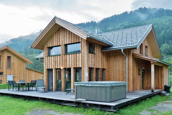 A wooden cabin with a deck, large windows, and a hot tub.