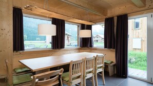 Un coin repas en bois, avec une grande table et des chaises, de grandes fenêtres avec des rideaux et une vue sur l’extérieur.