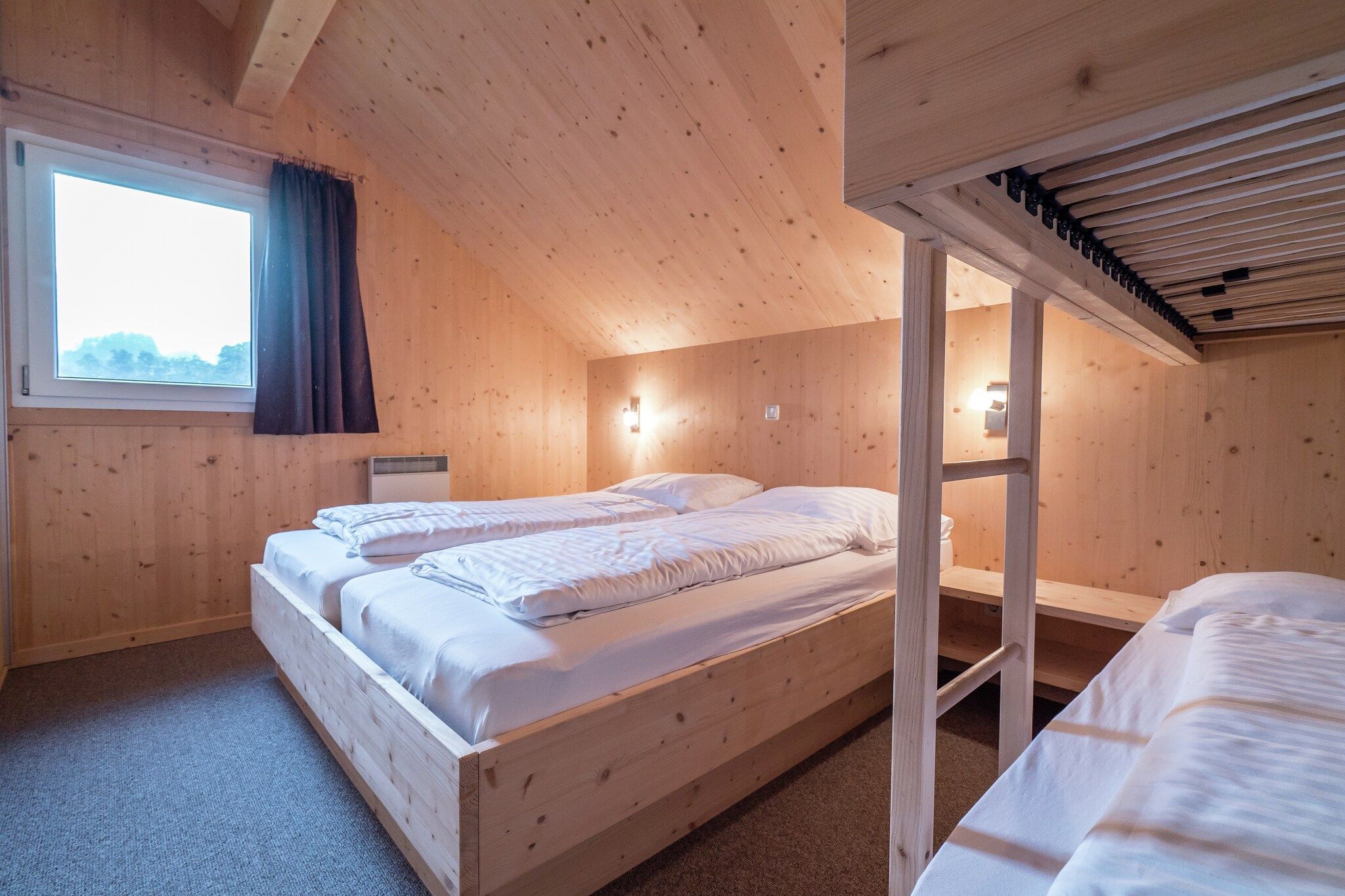 Una habitación de madera con una cama litera, una ventana con cortinas y una lámpara fijada a la pared.