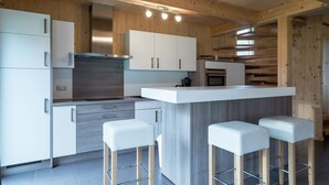 Une cuisine moderne avec des meubles blancs, un îlot central doté de tabourets et une hotte de cuisine en acier inoxydable.