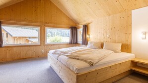 Une chambre dans une cabane en bois, avec un lit simple, deux fenêtres et un plafond en pente.