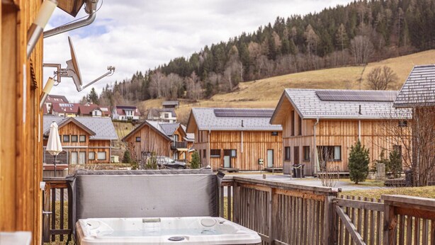 A wooden deck with a hot tub, overlooking a row of cabins with sloped roofs and solar panels. - Lovely chalet with whirlpool (Murau)