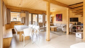 A spacious living area with a wooden ceiling, a dining table with chairs, a sofa, and a TV on a wooden stand. - Lovely chalet with whirlpool (Murau)