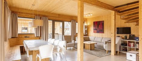 Un vaste espace de vie doté d’un plafond en bois, d’une table à manger avec des chaises, d’un canapé et d’un téléviseur posé sur un meuble en bois.