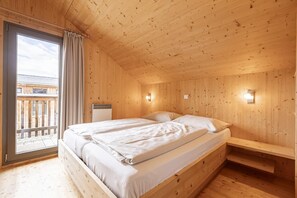 A wooden cabin room with a bed, a bench, and a window with curtains.
