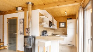 A modern kitchen with a central wood-burning stove, white cabinetry, and a small island with stools. - Lovely chalet with whirlpool (Murau)
