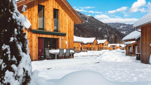 A wooden lodge with multiple cabins, a snow-covered landscape, and a mountain in the background.