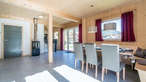 A modern wooden interior with a dining area, a sofa, and a view of the outside.