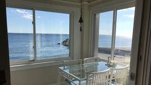 Un balcone con un tavolino in vetro e sedie bianche, con vista su una spiaggia e il mare.