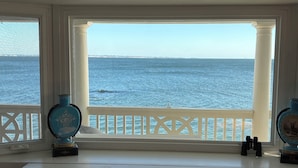 Una stanza con vista sul mare tramite un'ampia finestra, un corrimano bianco e due vasi decorativi su un tavolo consolle bianco.