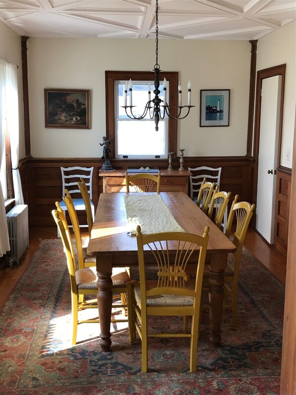 A dining room with a large wooden table, six chairs, a chandelier, and two framed pictures on the walls. - Waterfront beach house with arts and craft charm and views of Long Island Sound (New London)