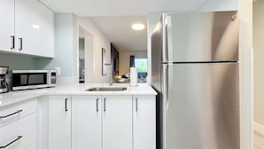 A modern kitchen with white cabinets, a stainless steel refrigerator, a microwave, and a coffee maker. - Sleek 1BR: Pool & Fashionable Design (Fort Lauderdale)
