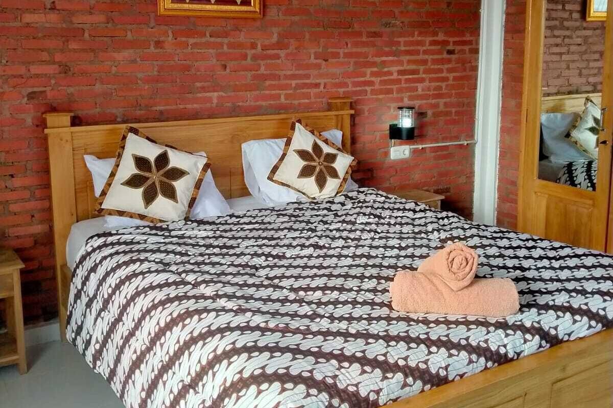 Un dormitorio con pared de ladrillo, estructura de cama de madera, ropa de cama estampada y un cuadro enmarcado sobre la cama.