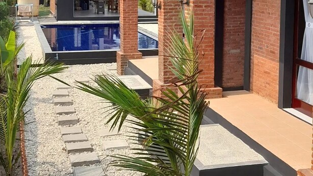Zona junto a la piscina con un edificio de ladrillo, una pileta y un patio cubierto.