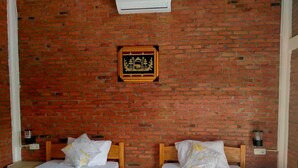 Una habitación con dos camas de madera, ropa de cama blanca, una pared de ladrillo y un cuadro enmarcado.