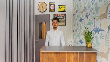 Un mostrador de recepción de hotel con un reloj, un cartel que indica política de salida las 24 horas y una pared con papel tapiz de temática de dinosaurios.
